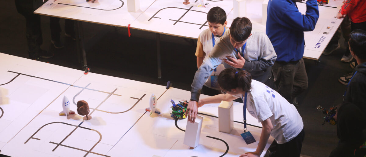 Un grupo de niños participando en la final de robótica educativa, trabajando con un robot en una mesa de circuito.