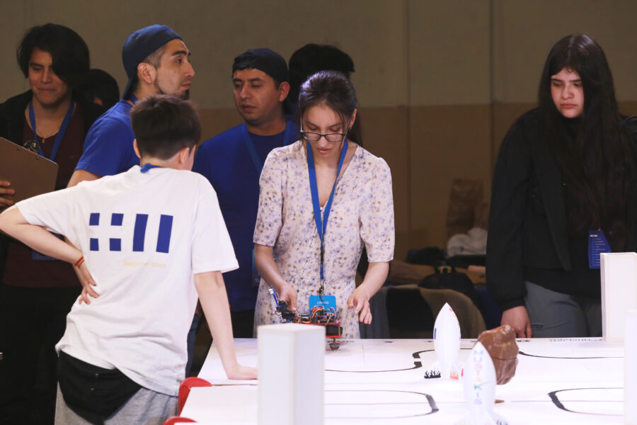 Grupo de niños y niñas participando de la final de robótica educativa. Una niña en particulpar se ve concentrada en la mesa.