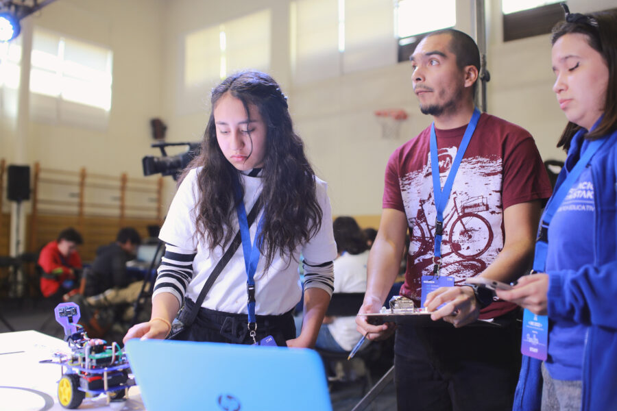 Grupo de niños y niñas participando de la final de robótica educativa. Están frente a un computador programando su robot.
