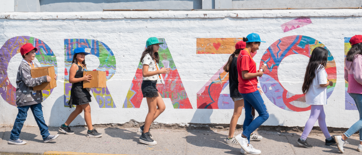 Un grupo de personas haciendo caminatas conscientes al aire libre. En la imagen se ven caminando frente a un mural que tiene escrito CORAZÓN en colores.