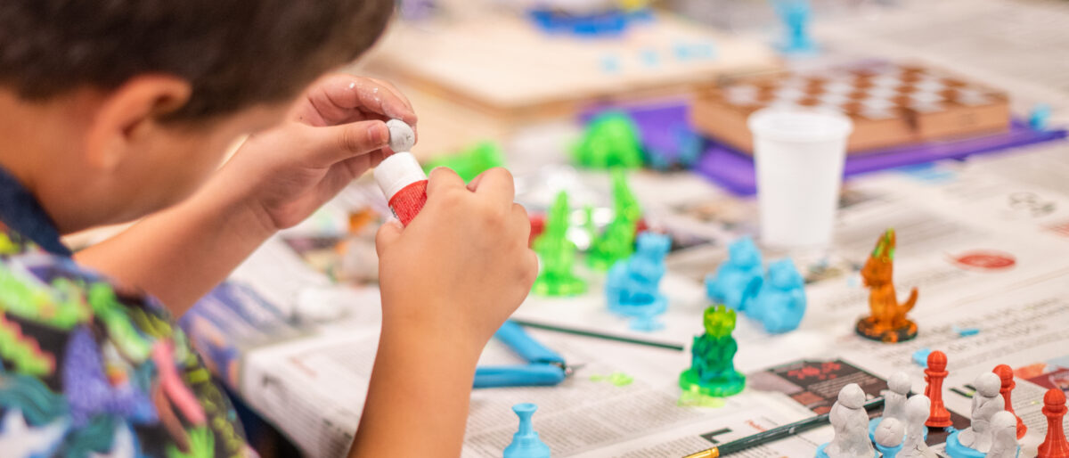 Un niño aprendiendo que nuestro cerebro se adapta al trabajar con figuras de goma y pegamento sobre un mesón de madera cubierto de periódicos.