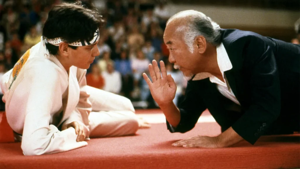 Escena de la película Karate Kid, el Señor Miyagi y su aprendiz, Daniel-San, sobre la importancia de aprender colaborativamente.